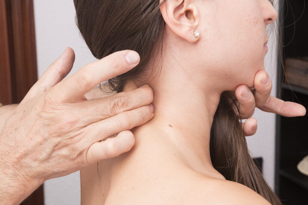 Il collo di una donna con capelli  lunghi mori e orecchino viene manipolato dalle dita  di un uomo per alleviare i sintomi da cervicale e vertigini.